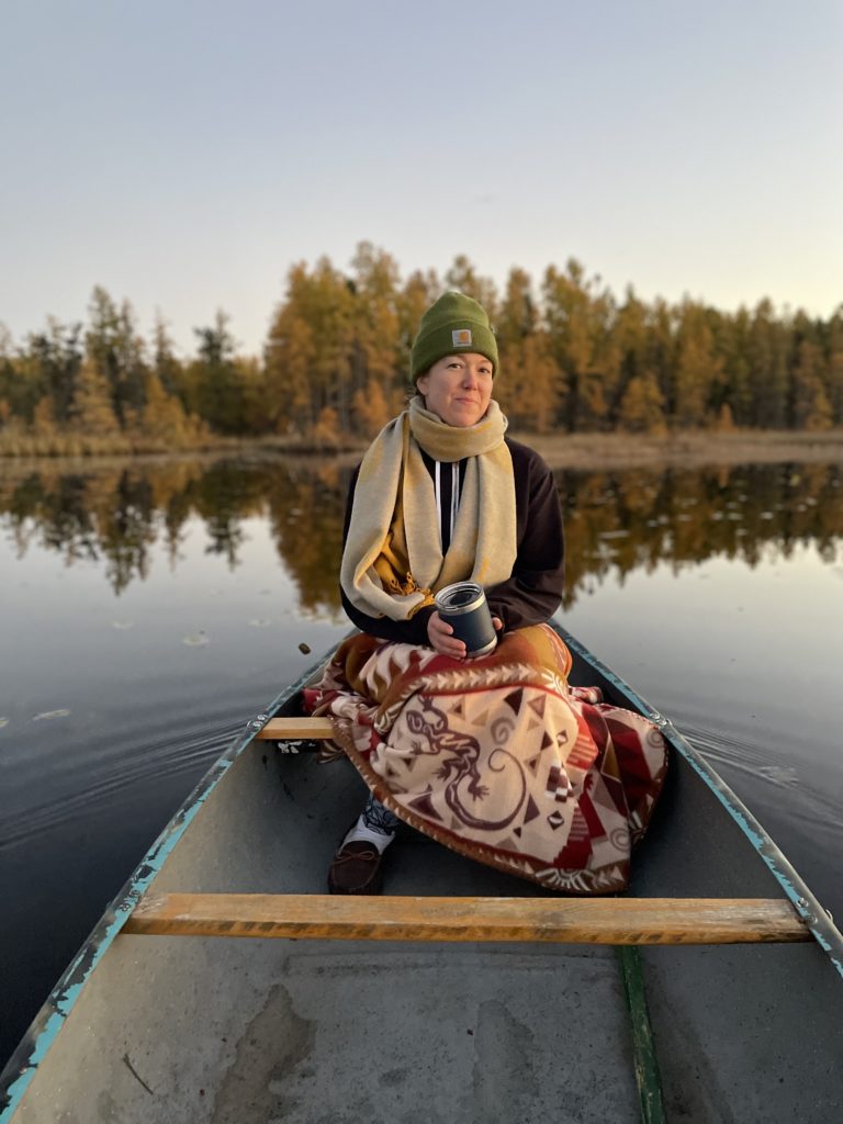 Amiable Properties, LLC proprietor Ami Stenseth, in a canoe at Ruby's cabin near Hinckley, MN and Danbury, WI, backed by golden tamaracks and colored fall leaves.